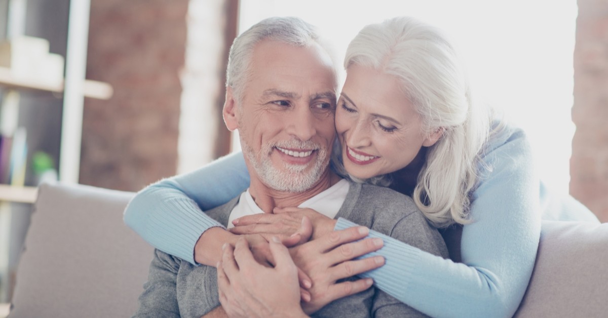 An elderly couple hugs while seated.